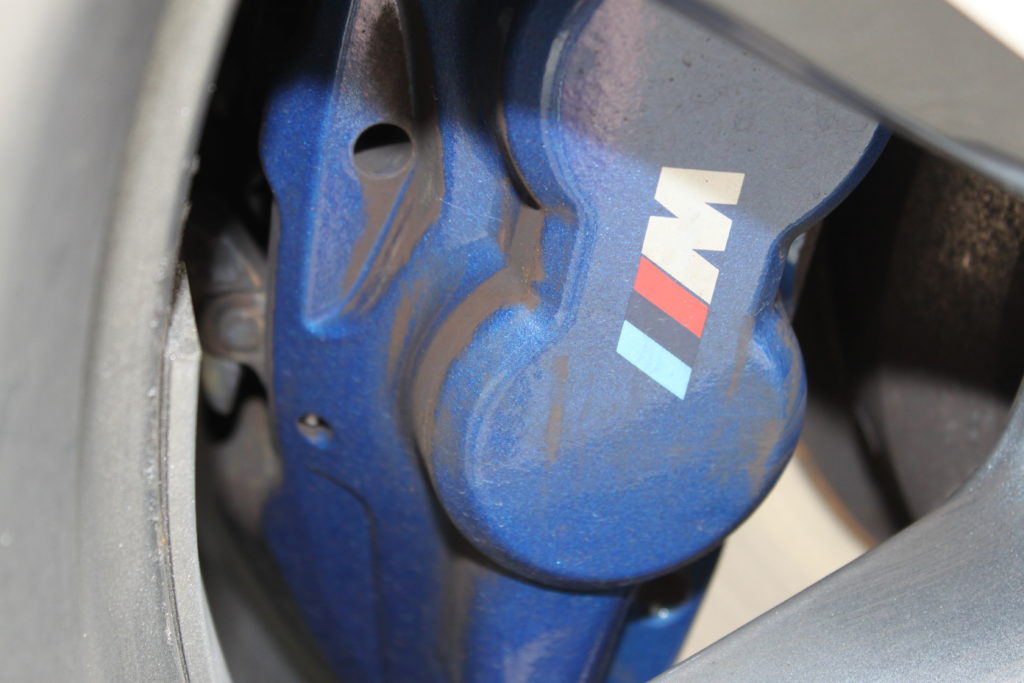 Blue brake caliper heavily with a heavy covering of brake dust